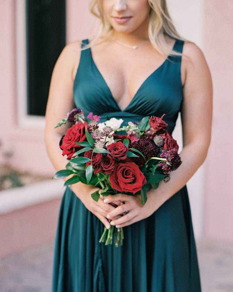 red wedding bouquet with jewel toned green bridesmaid dress